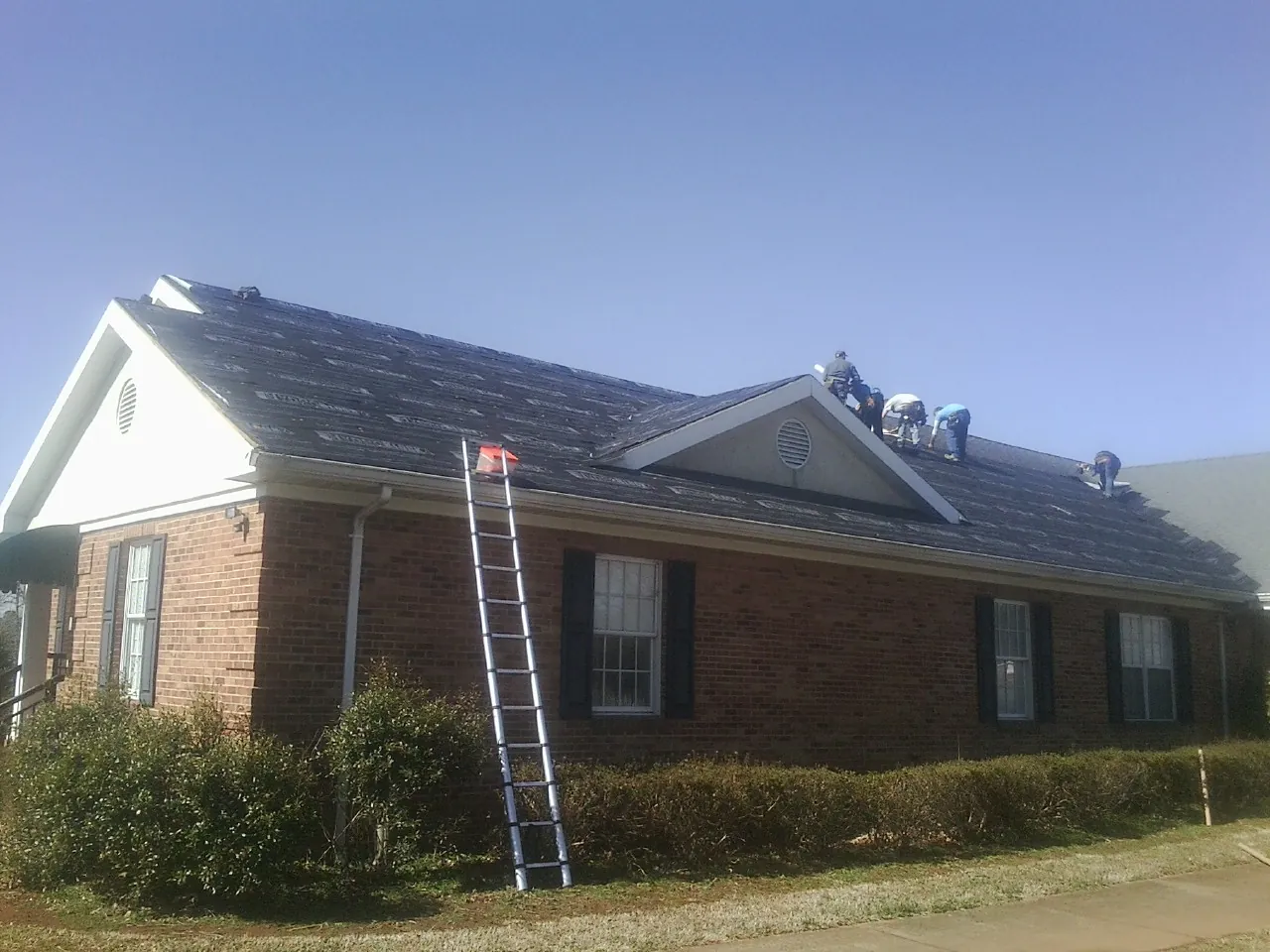 Crew tearing shingles off a brick ranch roof with a ladder set — Emergency Roof Repair work by our crew in Westport
